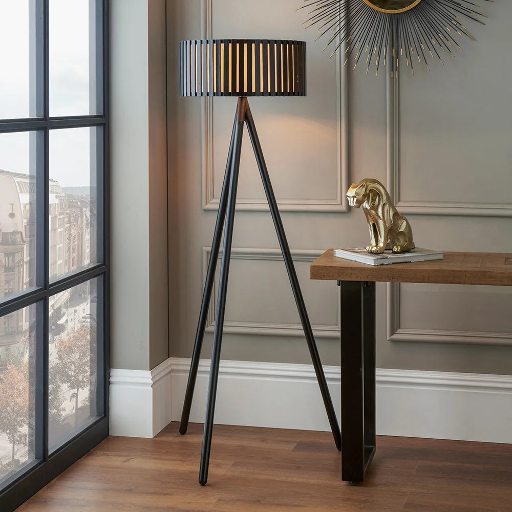 Rabanne slatted black wood tripod floor lamp in a small living room — distinctive slatted wood shade with black tripod base, warm geometric light pattern through slats